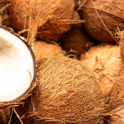 Heap of raw brown coconuts with a halved one showing the white flesh inside.